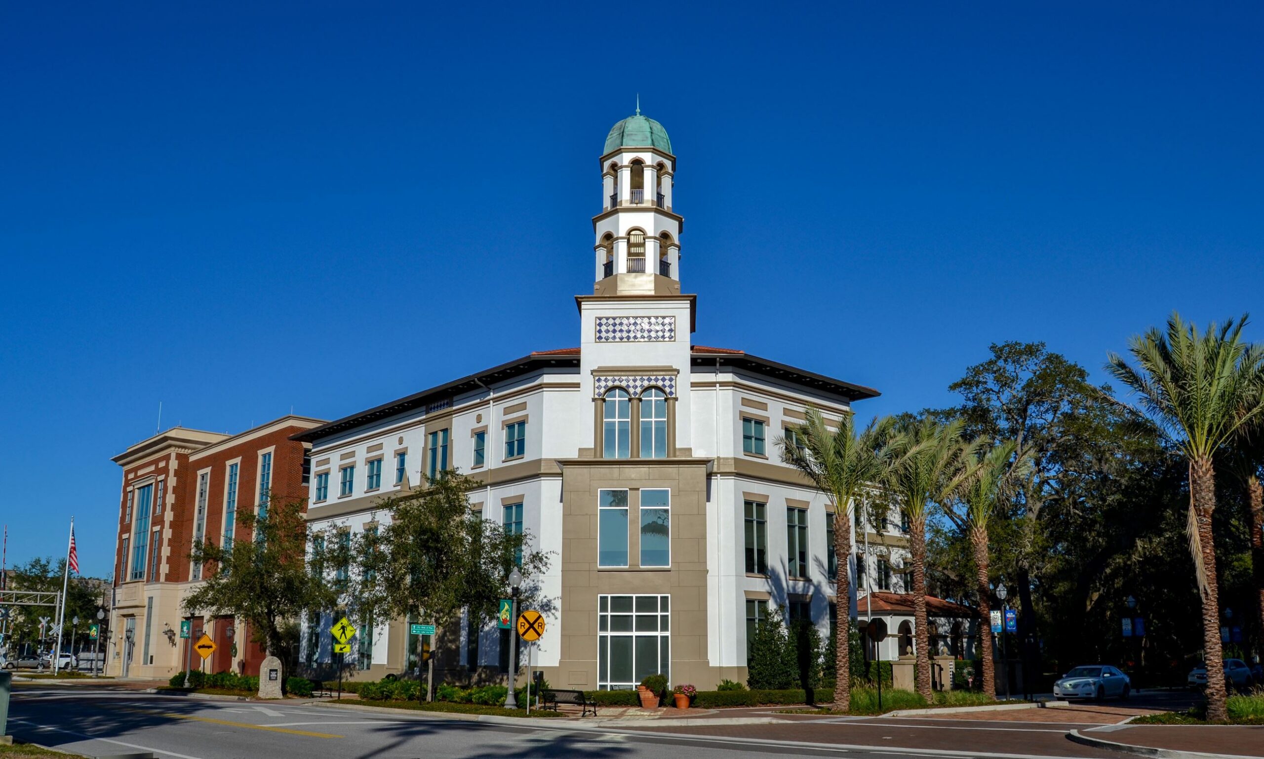 A three-story building with a decorative tower and dome stands at a street intersection lined with palm trees, traffic, and railroad signs under a clear blue sky—just move it into view for the perfect scene.