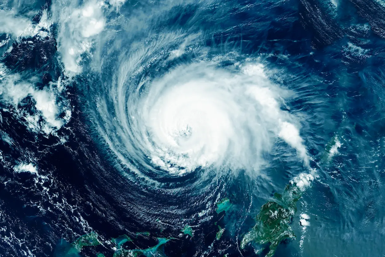 Satellite image of a large hurricane with a defined eye swirling over the ocean, approaching a landmass partially visible at the bottom right.